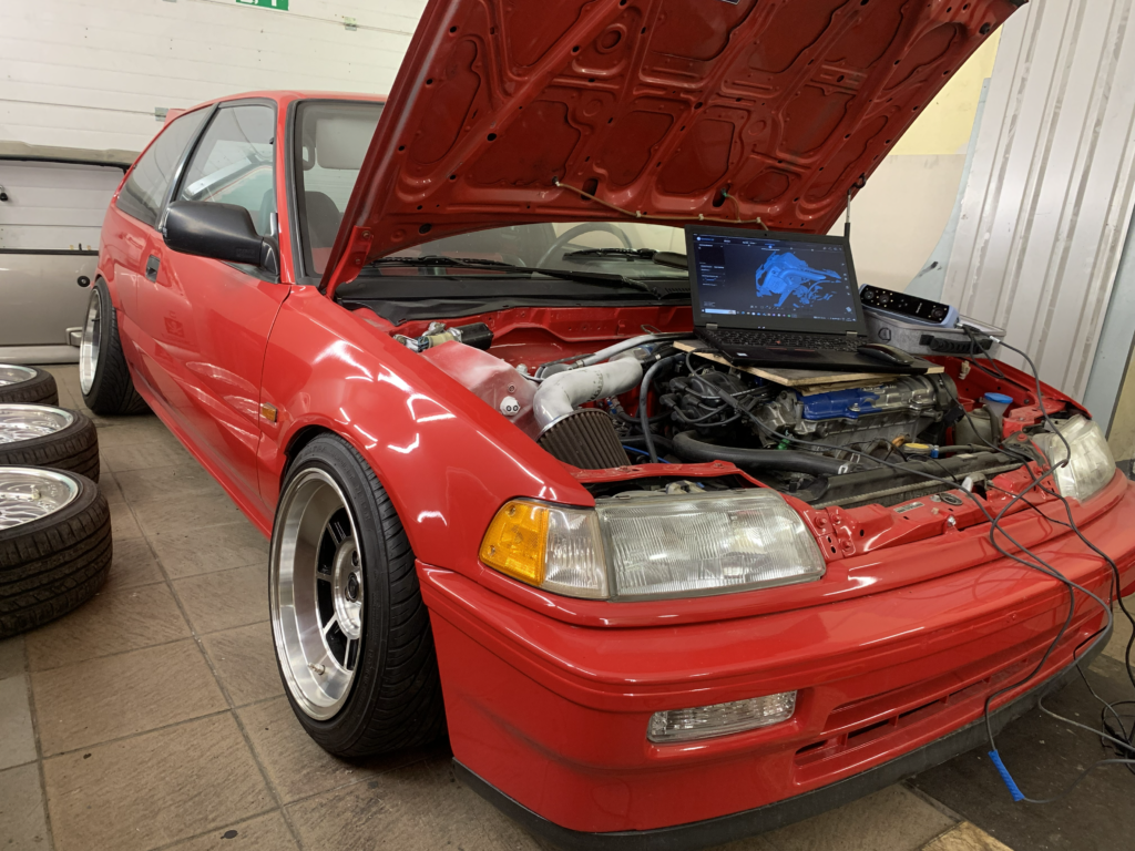 Avatud kapotiga auto mootoriruum, kus sülearvuti ekraanil on 3D-skaneering ja taustal skaneerimise seadistus.