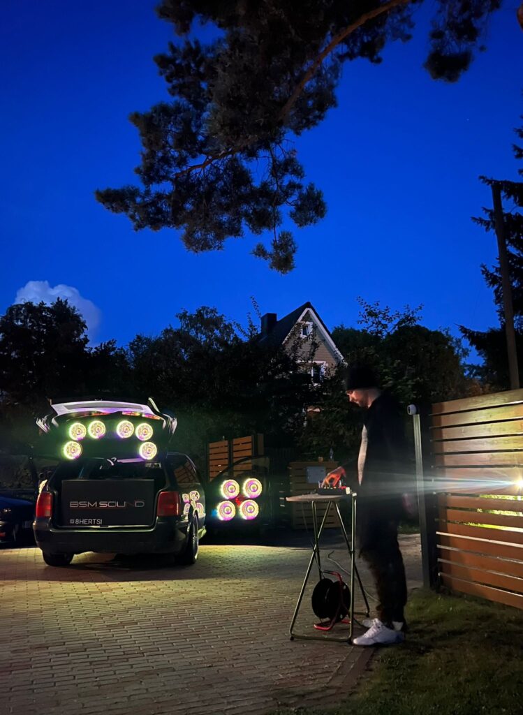 Õuealal auto pagasiruumis helisüsteem ja inimene helipuldi juures.